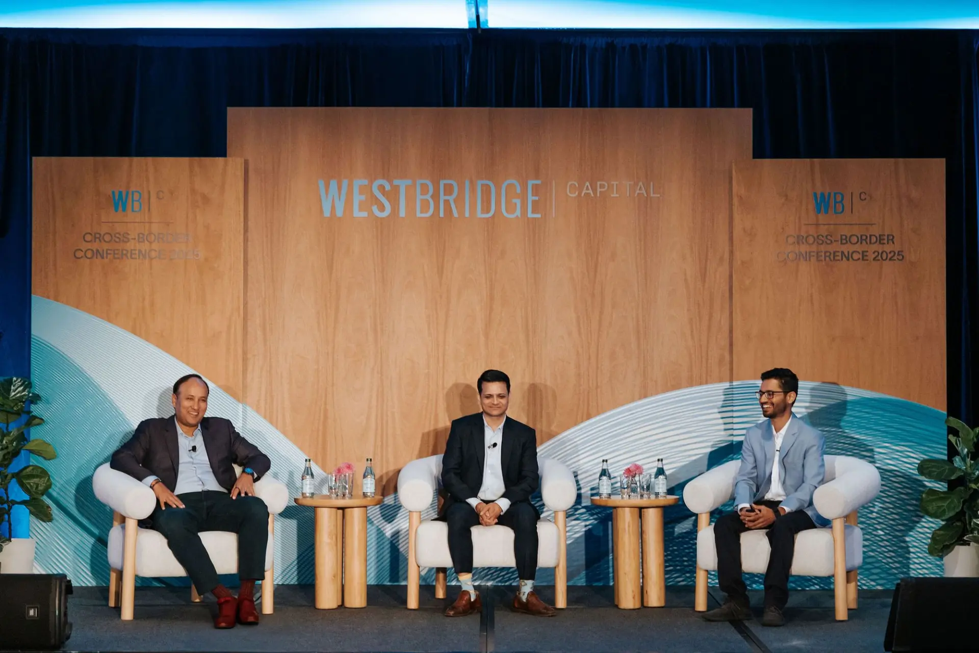 Three speakers in conversation on a WestBridge Capital conference stage